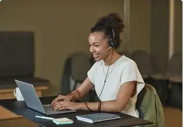Person smiling while working on a laptop and wearing a headset.